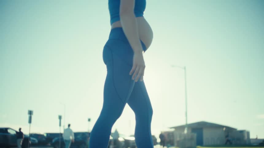 A young pregnant woman stretching outdoors on a grass lawn on a sunny day