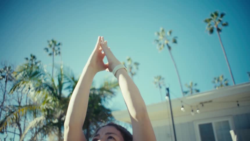 A view from the front shows a pregnant woman wearing a maroon sports bra and black leggings as she raises her arms during an outdoor workout in a sunny backyard