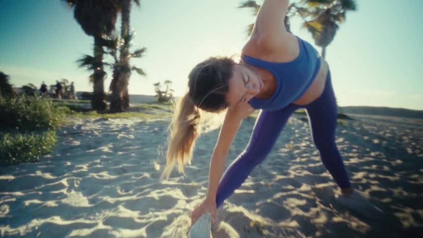 Woman leaning over with her arm in the air and bending down doing stretching exercises on the beach