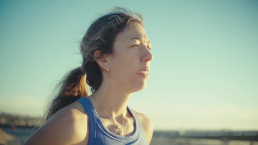 A woman stands outdoors during the golden hour looking thoughtfully toward the horizonshe is wearing a blue athletic tank top with her hair pulled back capturing a moment of quiet reflection or a pause during a workout
