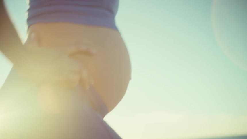 A pregnant woman in blue activewear walks on a sunny beach