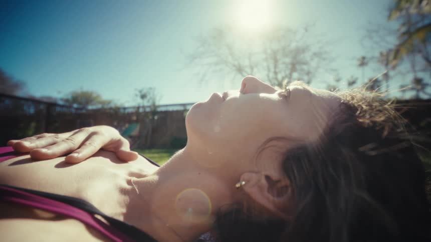 A woman lying on a mat relaxing in the sun in a grassy backyard