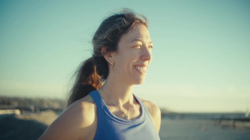 Sunlight shines on a woman standing along the coast with a smile on her face