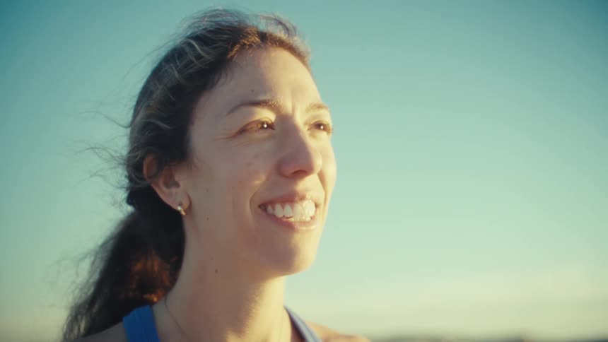 A pregnant woman jogs along a beach at sunset before stopping to smile