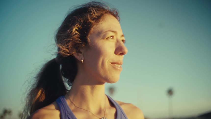 A young woman smiles softly while looking toward the sunlit horizon enjoying the warm glow outdoors