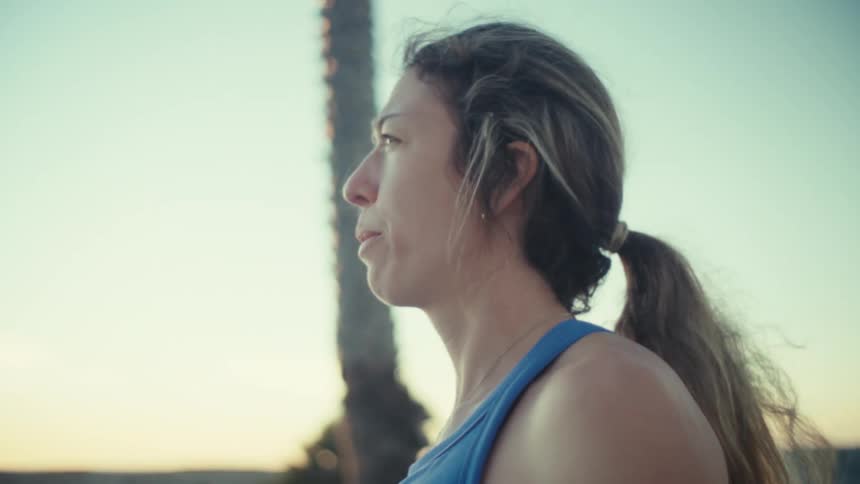 A young pregnant woman running outdoors at sunset stopping to catch her breath
