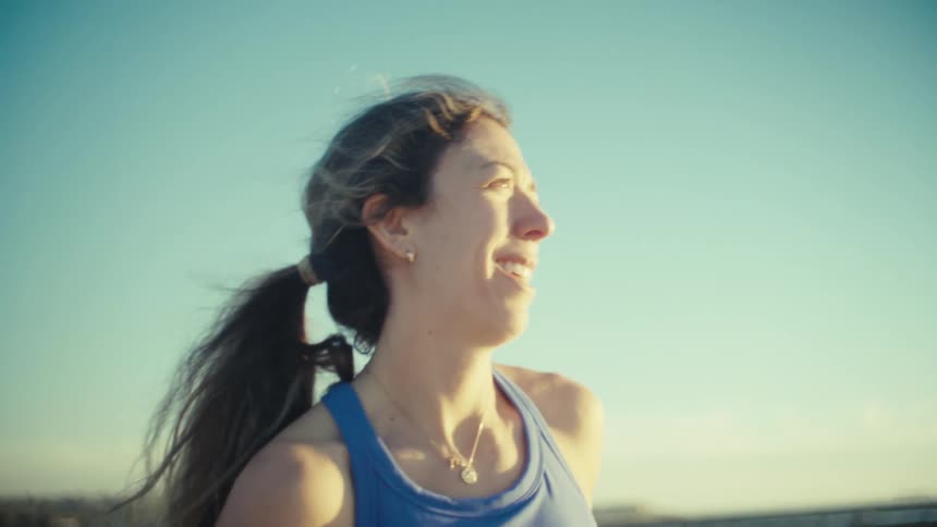A pregnant woman jogging along a sandy beach path under bright sunlight