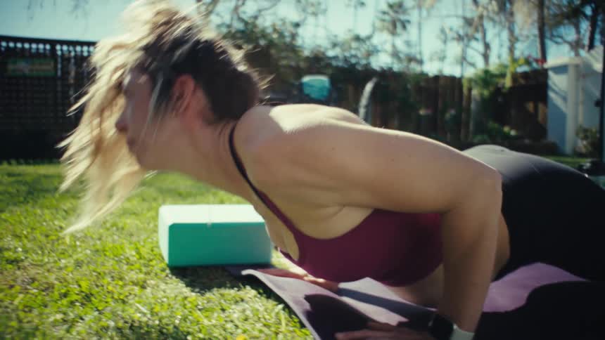 A pregnant woman practicing yoga on a mat in a sunny backyard