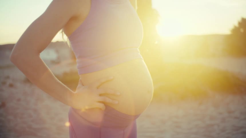 A pregnant woman standing outdoors catching her breath after exercise with her baby bump visible