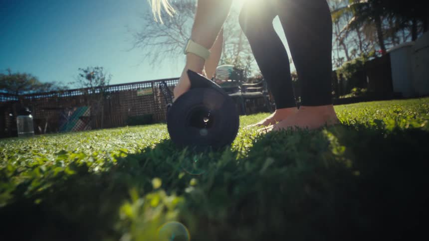 A pregnant woman spreading a yoga mat on her backyard lawn on a sunny day