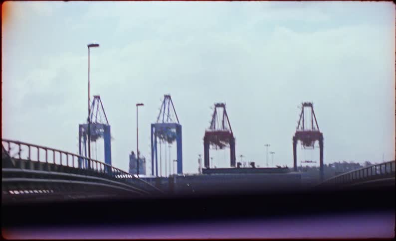 A dynamic view of industrial port cranes and a bridge from a moving vehicle