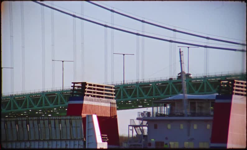 Vehicles move across a bridge as a large ship starts to go under the bridge