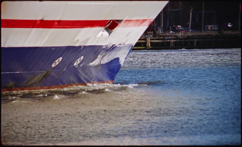 A large boat is moving through the water past piers