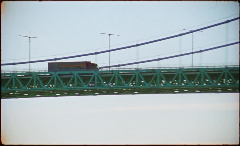 Red truck crosses green suspension bridge over river