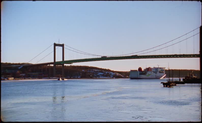 Suspension bridge spans a channel with a ferry sailing near the shoreline