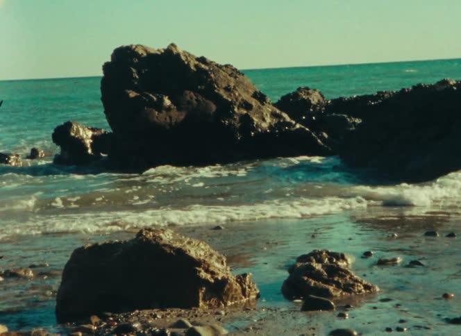 Dark rocks on the shoreline with gentle sea waves in the background