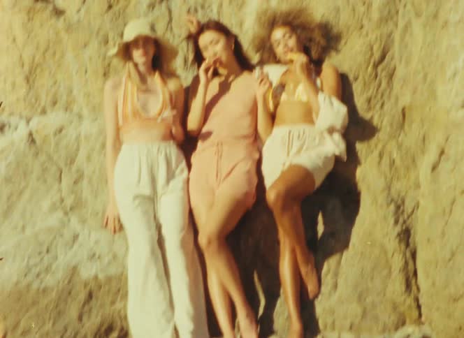 Three women leaning against a seaside rock hold make