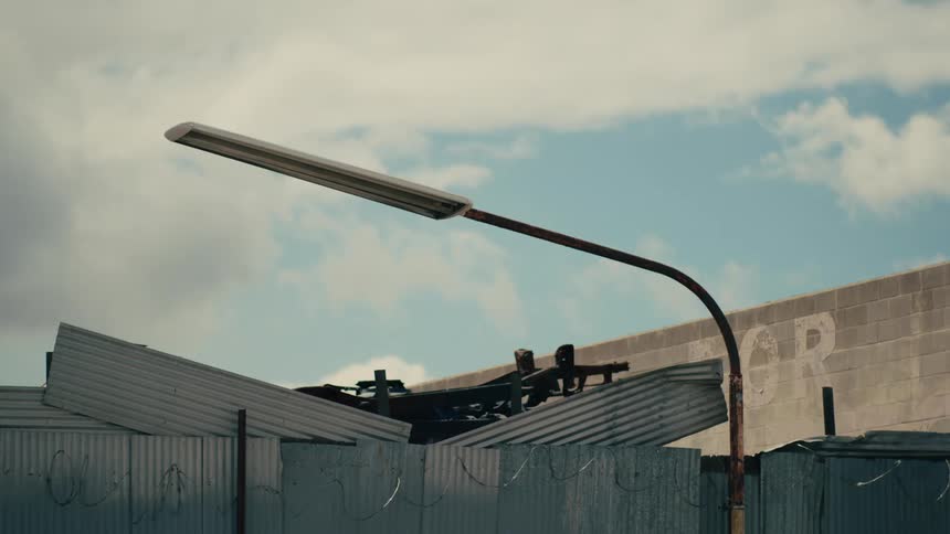Light pole in front of a dilapidated building as traffic moves by on the street