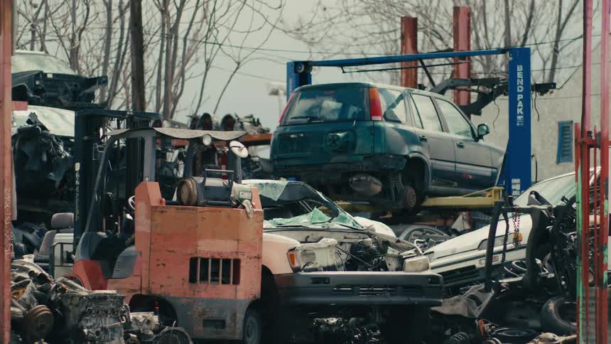 Traffic passes a junkyard containing wrecked cars and car parts on a winter day