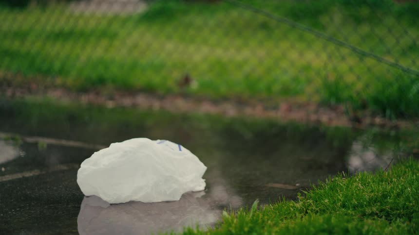 White plastic bag on a puddle beside grass and a chainlink fence