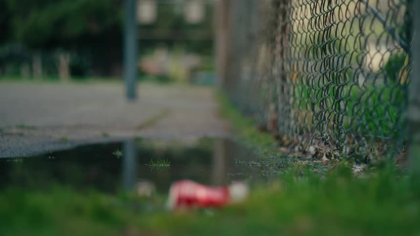 Chainlink fence beside sidewalk with a puddle reflecting the surroundings