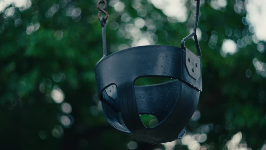 Empty baby swing sways back and forth on a summer day