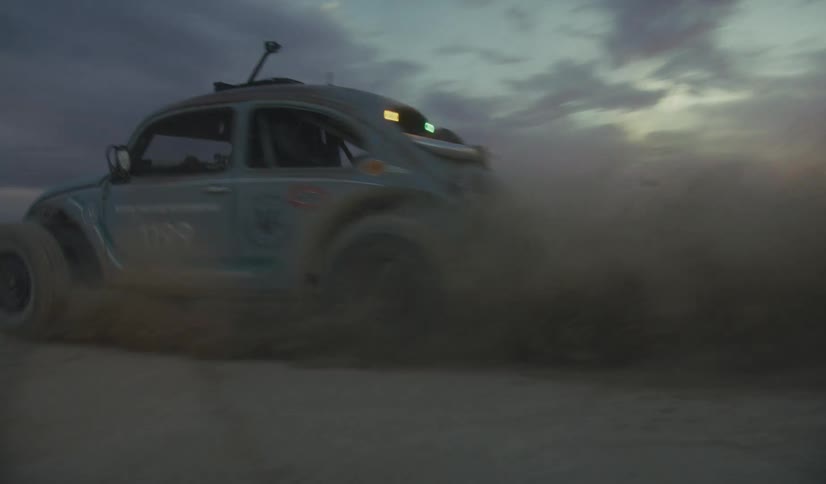 The car makes a turn in the sand causing a dust cloud