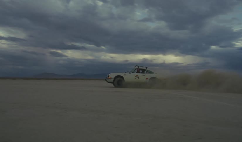 Car speeds across a desert plain casting sand into the air near sunset on a cloudy day