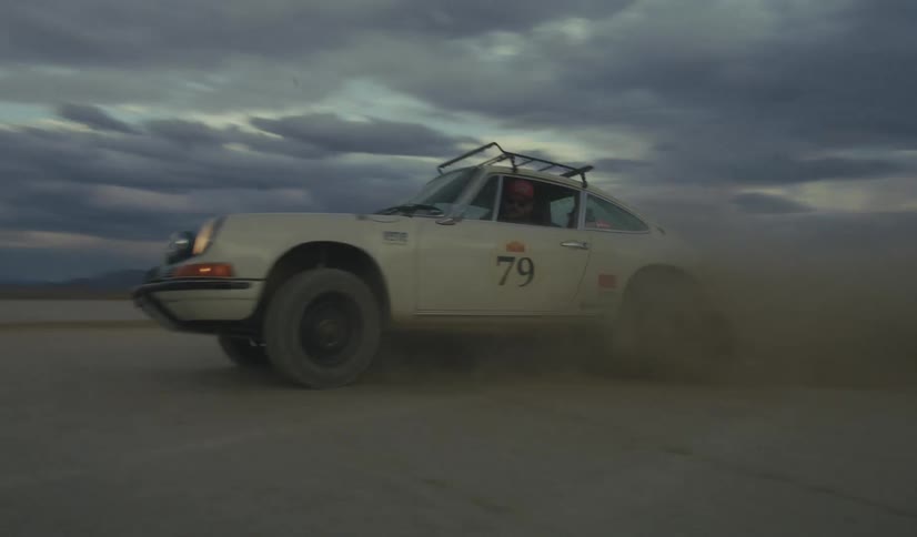 Rally car driving in the middle of the desert with mountains on the background during dusk or dawn