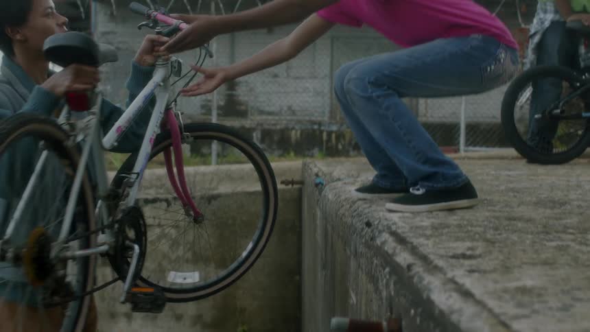 Two teenagers lift a bike up onto a concrete ledge in a city