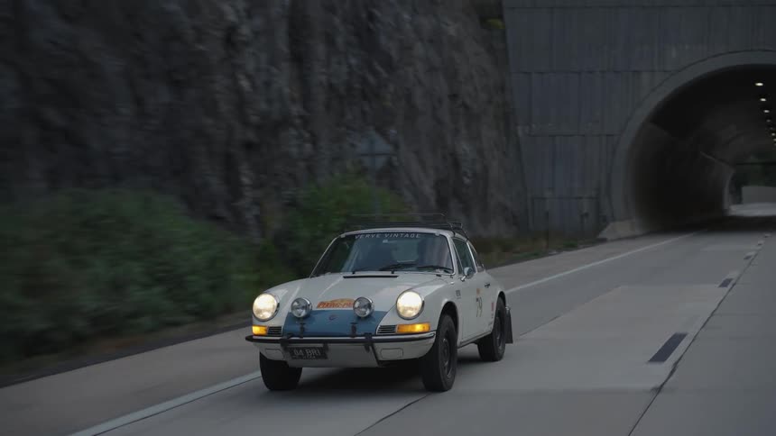 A white porsche race car exits a concrete tunnel on a mountain highway