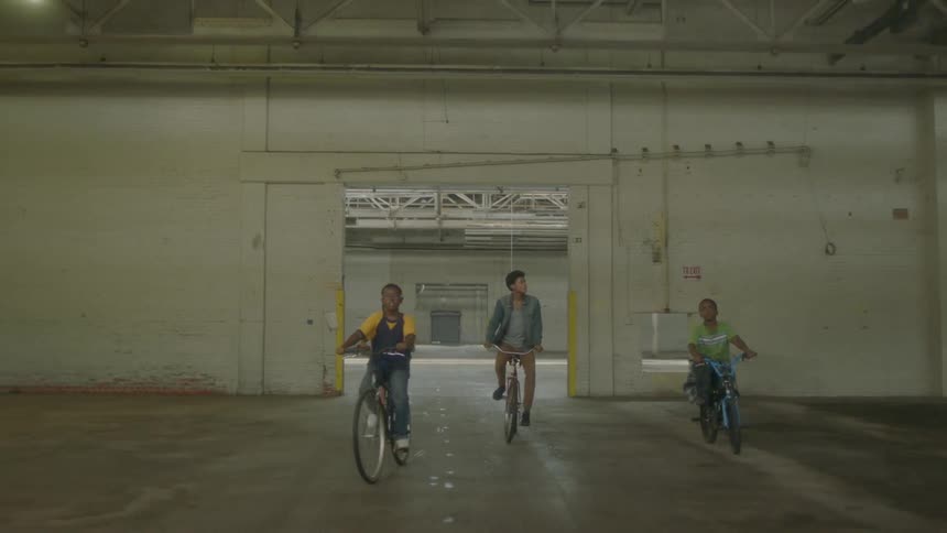 Boys ride bicycles in an empty warehouse
