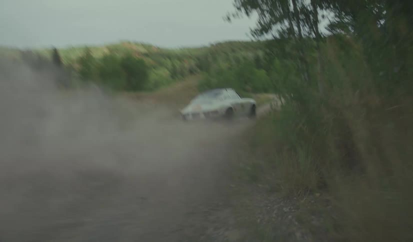 A sports car driving and drifting on a dirt road in the countryside at midday with trees and grass lining both sides of the road