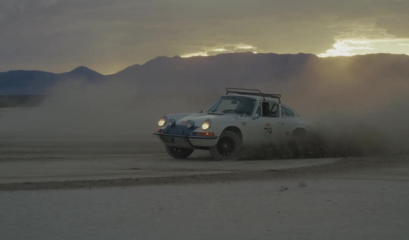 Car smokes as it turns and travels on a snow and ice covered road among mountains of snow under a cloudy winter sky