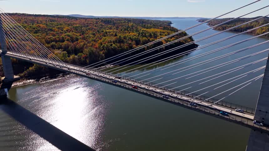 Vehicles cross a cablestayed bridge over a river with sunlight reflecting on the water