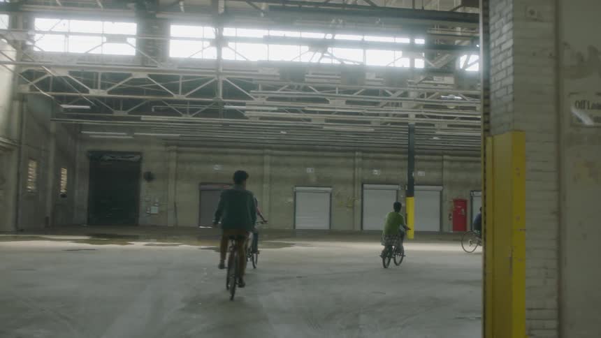 A group of kids ride their bikes in an abandoned factory