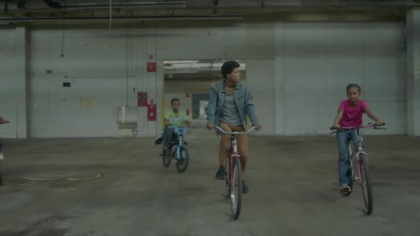 A group of kids ride bikes through a building