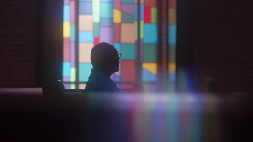 A man sits in front of stained glass in a chapel