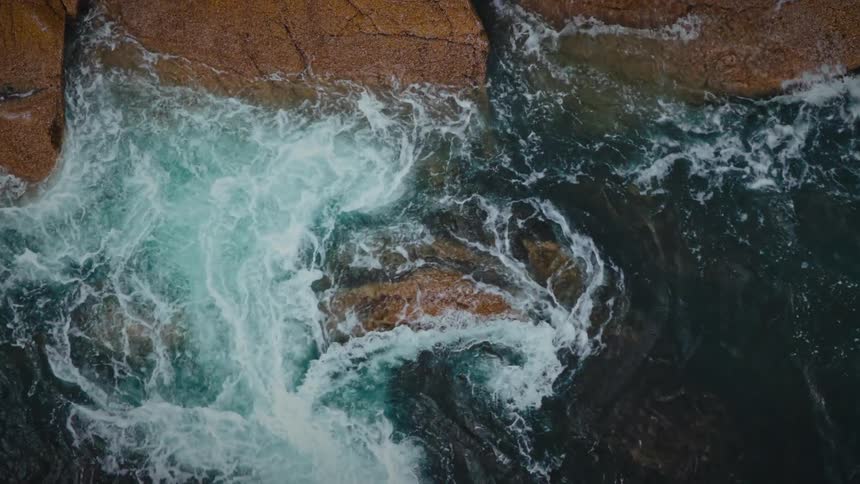 Ocean water crashing aggressively against a rock on the coastline at midday