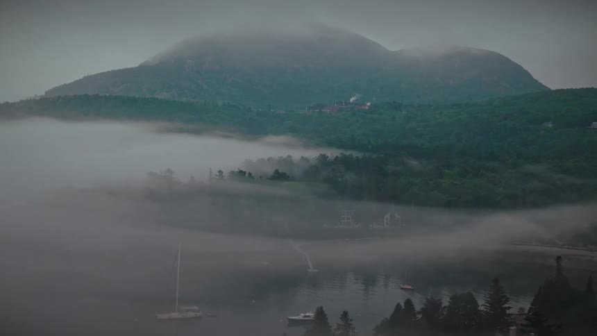 Fog covering a lake with boats and mountains in the background