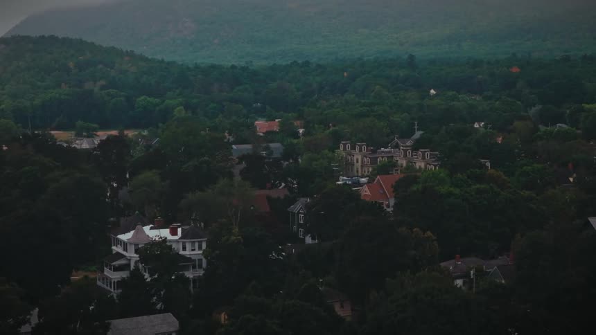 Light fog covers a heavily wooded residential neighborhood and the nearby forested mountain