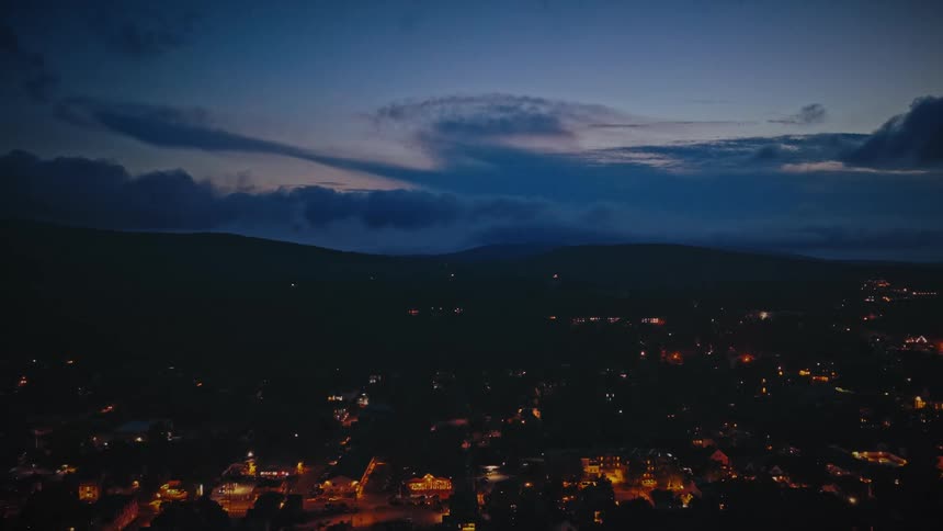 Aerial view moving over a town on high ground with lights on buildings glowing in the darkness