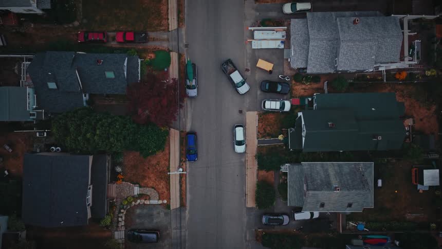 A city street view with cars parked along the roadside beside buildings as other cars drive by at midday