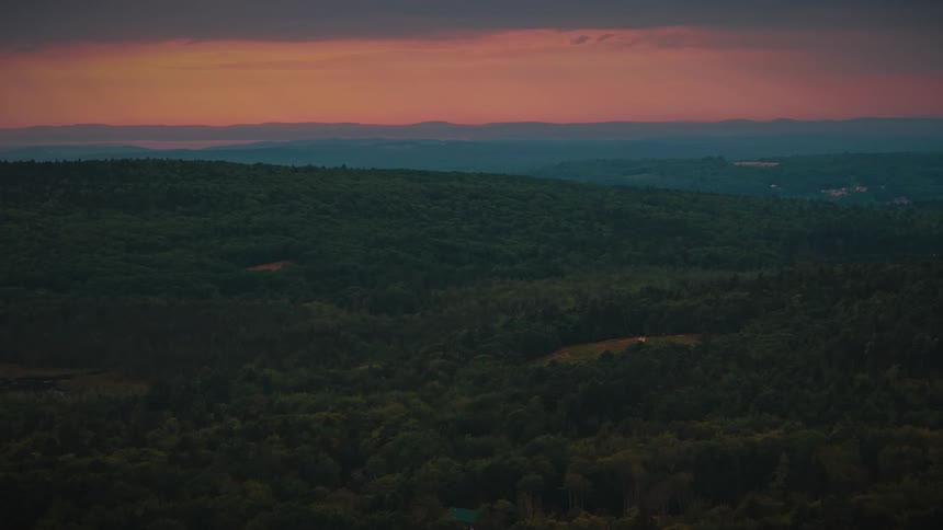 Forestcovered hills under an orange sky on the horizon