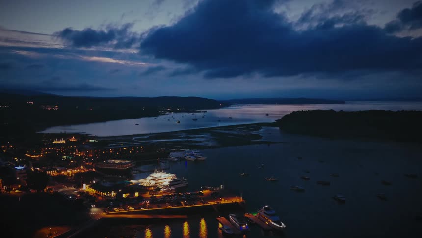 Marina lights reflect on the bay at dusk under dark clouds