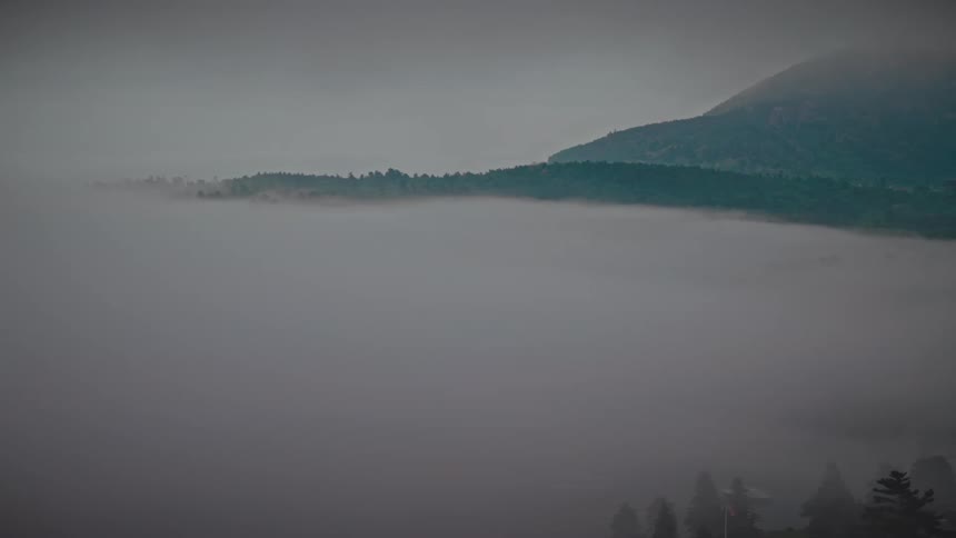 A thick blanket of fog fills the valley while a distant treelined ridge and a mistshrouded mountain rise above the haze