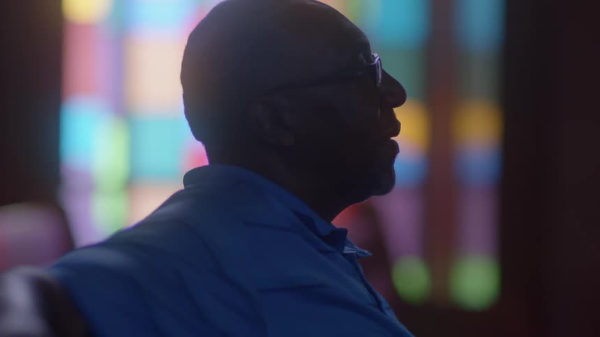 A man wearing glasses sits in a church