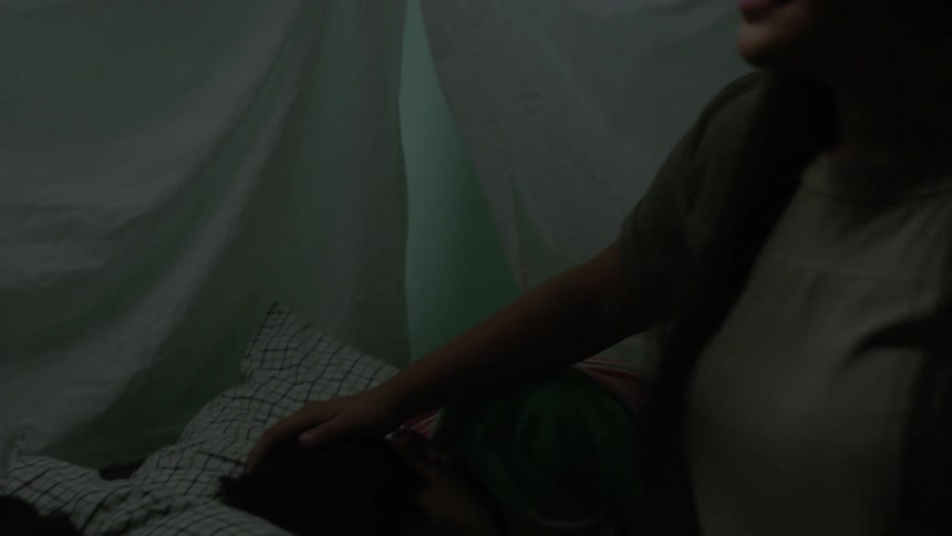 A woman is sitting near a sleeping child and smiling