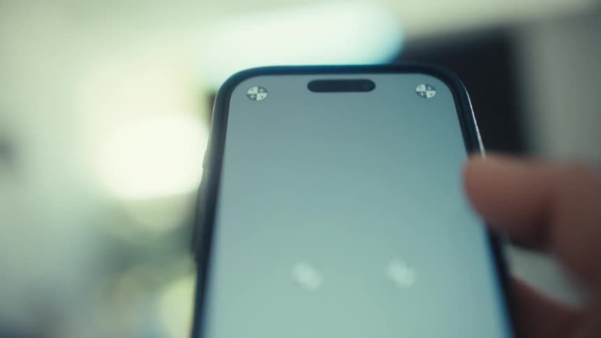 A person holds a dark smartphone with a light gray screen displaying tracking markers while standing in a dimly lit room