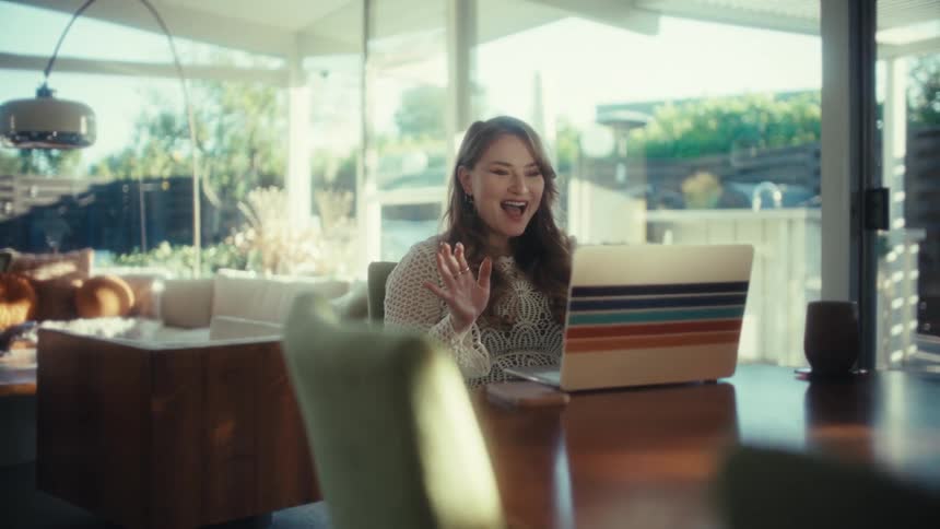 A woman happily waving at a laptop